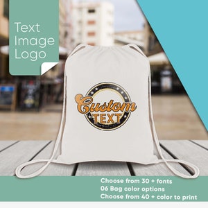 Op de afbeelding: Witte trekkoordtas met een aangepast tekstontwerp. Het ontwerp heeft een cirkel met de woorden "Custom Text" in oranje en zwarte letters. De tas is gemaakt van katoen en heeft een wit trekkoord.