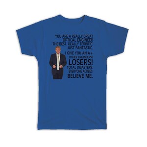 May include: A royal blue t-shirt with a humorous graphic. The graphic includes a picture of a man in a suit and tie, along with text that reads: "YOU ARE A REALLY GREAT OPTICAL ENGINEER...LOSERS! BELIEVE ME."