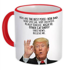 Puede incluir: Taza de café de cerámica blanca con borde rojo. La taza presenta una foto de Donald Trump y el texto "You are the best Pixie-Bob Dad. Very special. Very talented. Really terrific. High IQ. Other cat dads? Fake news. Believe me."