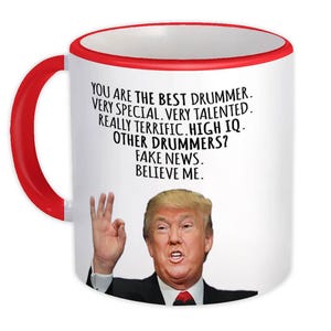 Könnte beinhalten: Ein weißer Keramikbecher mit rotem Henkel und Rand, der eine Grafik von Donald Trump zeigt, der eine Handgeste macht. Der Text lautet: YOU ARE THE BEST DRUMMER. VERY SPECIAL. VERY TALENTED. REALLY TERRIFIC. HIGH IQ. OTHER DRUMMERS? FAKE NEWS. BELIEVE ME.