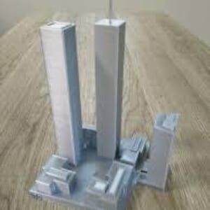 Könnte beinhalten: Ein graues 3D-gedrucktes Modell der Twin Towers in New York City. Das Modell umfasst die Türme, die umliegenden Gebäude und eine kleine Antenne auf der Spitze des höheren Turms.