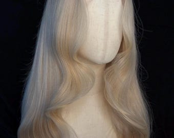 May include: A long, light blonde wig with soft waves and a natural-looking hairline. The wig is styled on a mannequin head against a dark background, showcasing its length and volume. The hair has a subtle gradient of color.