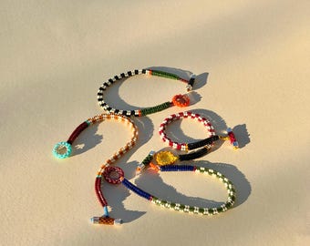 May include: Four beaded bracelets featuring intricate patterns of small glass beads in various colors including green, black, white, orange, yellow, blue, and maroon. Each bracelet includes a toggle clasp closure with a silver-toned metal bar.