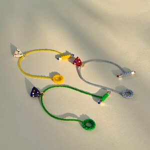 May include: Three beaded necklaces in yellow, gray, and green. Each necklace features a different geometric shape: a triangle, a circle, and a cylinder. The triangles are decorated with colorful beads, and the circles and cylinders are also beaded.