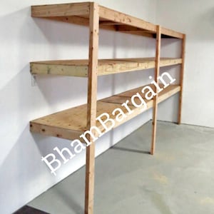 Puede incluir: Una estantería de madera con tres estantes, montada en una pared. Los estantes están hechos de madera contrachapada y los soportes están hechos de madera maciza. La unidad está sin terminar y tiene un color de madera natural.