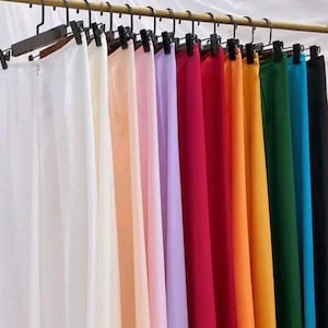 May include: A collection of 12 long, flowing skirts in various colors, hanging on a rack. The skirts are made of a lightweight fabric and have a simple, elegant design.