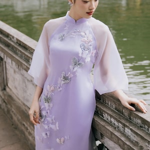 May include: A lavender silk dress with a sheer overlay and butterfly embroidery. The dress has a mandarin collar and a long, flowing skirt.