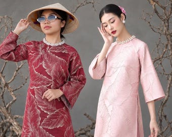 May include: Two long-sleeved tunics featuring a textured leaf pattern. One tunic is deep red with gold-toned leaf details, worn with a conical straw hat and sunglasses. The other is light pink with matching leaf textures and a pearl necklace.