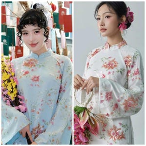 May include: Two women wearing traditional light blue and white floral dresses with long sleeves. The dresses have a mandarin collar and are adorned with sequins. One woman holds a bouquet of flowers.