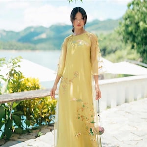 May include: A yellow dress with floral embroidery and sheer sleeves. The dress is long and has a simple, elegant design.