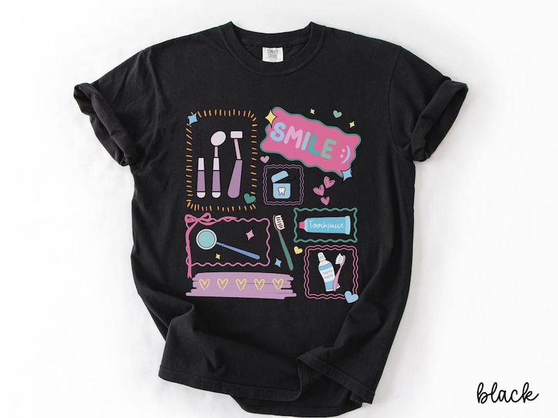 Op de afbeelding: Een zwart t-shirt met een kleurrijke grafische print van tandheelkundige instrumenten, waaronder een spiegel, tandenborstel en tandpastatube. Het ontwerp bevat de tekst "SMILE :)" in een roze tekstballon, omringd door kleine hartjes en kaders.