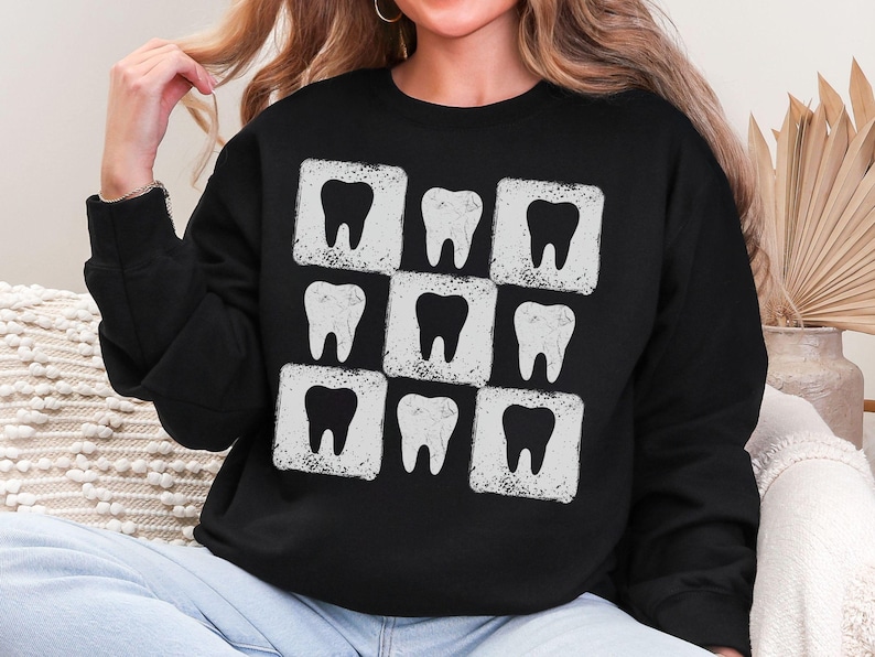 K&ouml;nnte beinhalten: Schwarzes Sweatshirt mit einem sich wiederholenden Muster aus wei&szlig;en Z&auml;hnen in wei&szlig;en quadratischen Rahmen. Die Z&auml;hne haben ein verwittertes, Vintage-Aussehen. Das Sweatshirt ist ein Rundhals-Modell und aus weichem Material.