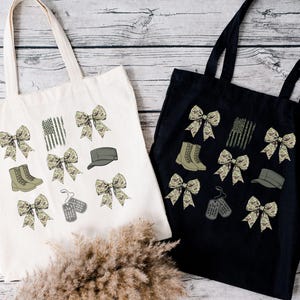 May include: Two tote bags with different colored fabric. One is white with camouflage print bows, boots, a hat, and dog tags. The other is black with camouflage print bows, boots, a hat, and dog tags.