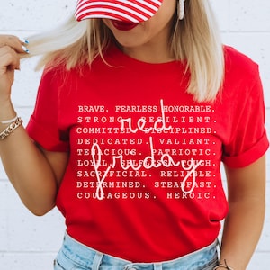 May include: A red t-shirt with the words "Red Friday" in a handwritten font. The shirt also lists several positive attributes in a white font, including "brave," "fearless," and "honorable."