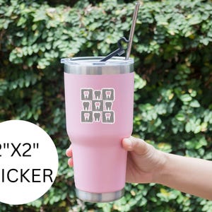 K&ouml;nnte beinhalten: Ein rosa isolierter Becher mit einem Edelstahlstrohhalm und einem schwarzen Strohhalterschutz. Der Becher hat einen Aufkleber mit einem Raster aus grauen Zahn-Symbolen. Der Aufkleber ist mit "2"X2" STICKER" beschriftet.
