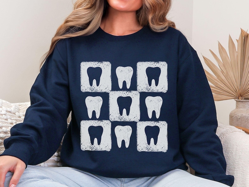 K&ouml;nnte beinhalten: Marineblaues Sweatshirt mit einem sich wiederholenden Muster aus neun wei&szlig;en Zahngrafiken. Jeder Zahn befindet sich in einem wei&szlig;en Quadrat, wodurch ein Raster entsteht. Das Design hat einen leicht verwitterten, Vintage-Look. Das Sweatshirt ist ein l&auml;ssiges, bequemes Kleidungsst&uuml;ck.