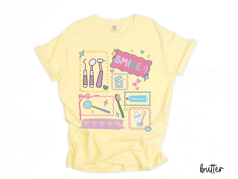 Op de afbeelding: Een lichtgeel t-shirt met een kleurrijke grafische print van tandheelkundige instrumenten, waaronder een spiegel, sonde, tandenborstel en tandpasta. Het ontwerp bevat de tekst "SMILE :)" in een roze tekstballon, omringd door kleine hartjes en sterren.