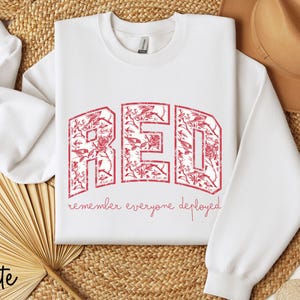 May include: White sweatshirt with the word "RED" in a floral design. The text "remember everyone deployed" is below the word "RED". The sweatshirt has long sleeves and a crew neck.