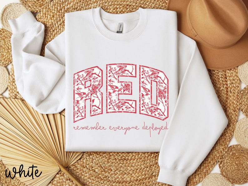 May include: White sweatshirt with the word "RED" in a floral design. The text "remember everyone deployed" is below the word "RED". The sweatshirt has long sleeves and a crew neck.