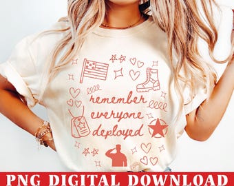 May include: Cream-colored t-shirt with a red graphic design. The design includes a flag, hearts, stars, a military boot, dog tags, and a saluting soldier. The words "remember everyone deployed" are also in the design.