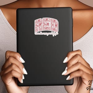 May include: A black tablet with a red sticker that says "RED" in a decorative font. The sticker also has the text "remember everyone deployed" in a script font. The sticker is 2" x 2".