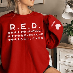 May include: Red sweatshirt with the text "R.E.D. REMEMBER EVERYONE DEPLOYED" and stars printed on the front. The left sleeve has the word "NOSTALGIA" printed on it.