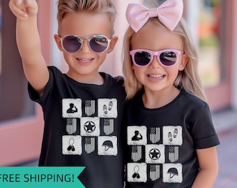 May include: Two children wearing black t-shirts with a white design of American flags, stars, and military symbols. The boy is wearing sunglasses and the girl is wearing a pink bow in her hair.