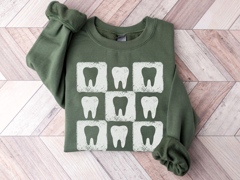K&ouml;nnte beinhalten: Gr&uuml;nes Sweatshirt mit einem wei&szlig;en Zahnmotiv, das in einem Rastermuster wiederholt wird. Die Z&auml;hne befinden sich in einem quadratischen Rahmen mit einem Used-Look. Das Sweatshirt hat einen Rundhalsausschnitt und lange &Auml;rmel.