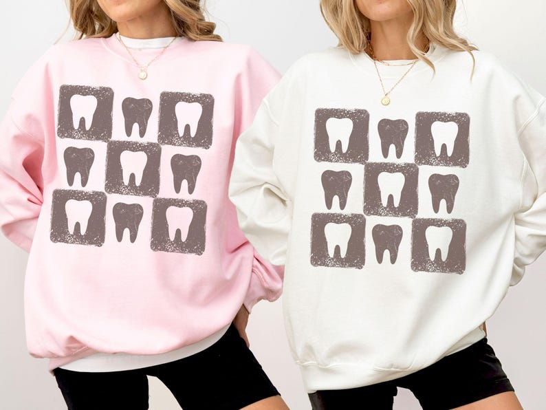 K&ouml;nnte beinhalten: Zwei Sweatshirts, eines rosa und eines wei&szlig;, jeweils mit einem sich wiederholenden Muster aus Z&auml;hnen in quadratischen Rahmen. Die Z&auml;hne sind in einem ged&auml;mpften Braun gehalten, und die Sweatshirts haben einen Rundhalsausschnitt.
