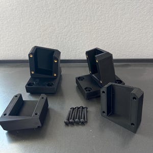 May include: A collection of black, geometric-shaped mounting brackets and screws. The brackets are made of a matte black material and have pre-drilled holes for screws. The screws are also black and appear to be made of metal.