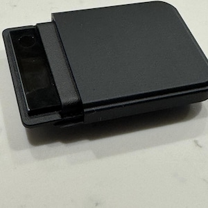 Könnte beinhalten: Eine rechteckige, schwarze Digitalwaage mit glatter, matter Oberfläche und einem kleinen, dunklen Display auf der linken Seite. Das Gerät verfügt über abgerundete Ecken und eine flache, solide Oberfläche in einem kompakten, funktionalen Design.