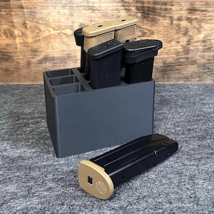 May include: A black plastic magazine holder with five slots for storing magazines. The holder is filled with four tan and black magazines.