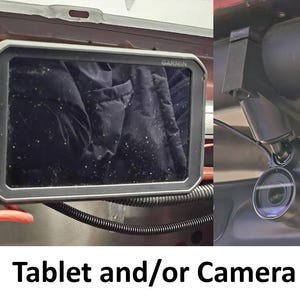 May include: A black Garmin tablet installed in a vehicle dashboard, next to a black camera system. The tablet is rectangular with a black frame. The camera has a lens and is mounted on a black bracket. The text "Tablet and/or Camera" is at the bottom.