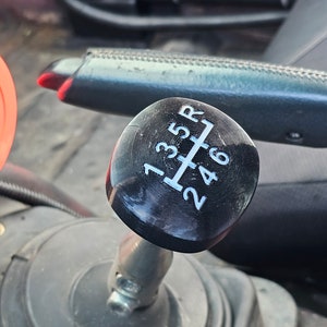 May include: Black gear shift knob with white numbers 1, 2, 3, 4, 5, 6, and R printed on the top.