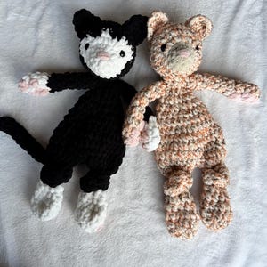 May include: Two crocheted stuffed cat toys. One is black with white accents and the other is orange and white.
