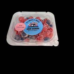 Puede incluir: Un recipiente de plástico transparente lleno de caramelos agrios de fresa y arándano. El recipiente tiene una etiqueta que dice "A's Sweets & Treats Sour Gushers Net Wt 8 oz (453,59 g)". Una pegatina rosa con el texto "Pink Lemonade" está en el lateral del recipiente.