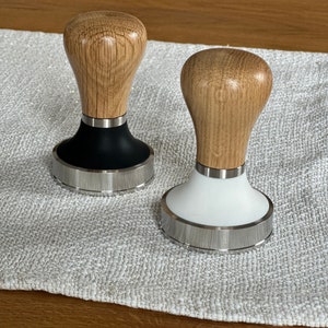 Könnte beinhalten: Zwei Kaffeettamper aus Holz mit schwarzer und weißer Basis. Die Tamper haben einen Holzgriff und eine Basis aus Edelstahl.