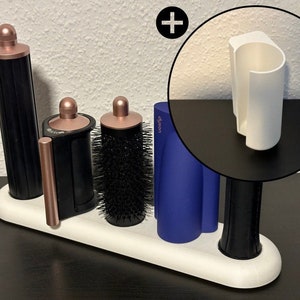 May include: A white stand with five slots for hair styling tools. The stand has a rose gold, black, and blue hair styling tools. The stand is on a black surface.