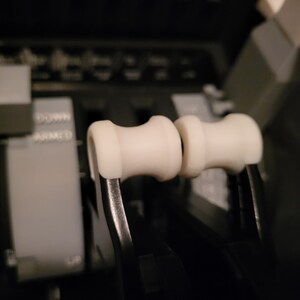 May include: Close-up of two white plastic knobs on black levers. The levers are labeled "DOWN" and "ARMED".