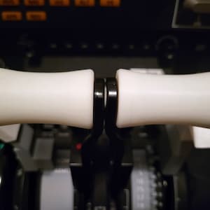May include: Close-up of a pair of white, cylindrical handles attached to a black metal base. The handles are smooth and have a slight curve.