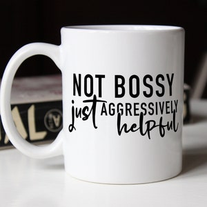 Puede incluir: Taza de café de cerámica blanca con texto negro que dice "No mandona, solo agresivamente servicial".