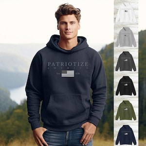 May include: A navy blue hooded sweatshirt with the text "PATRIOTIZE AMERICA" and a graphic of the American flag. The sweatshirt has a front pocket and is displayed on a person wearing blue jeans. Additional sweatshirts in white, gray, black, olive, navy, and red are also shown.