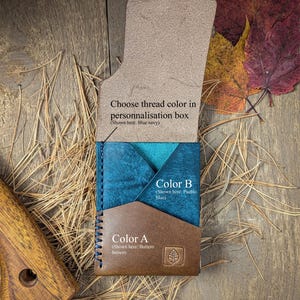 May include: A leather card holder featuring a brown front pocket labeled Color A, a blue middle pocket labeled Color B, and an open flap with text reading Choose thread color in personnalisation box. The stitching is blue navy.