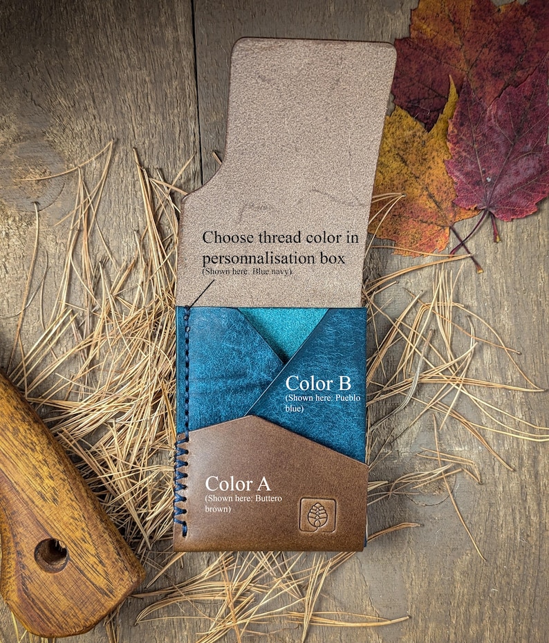 May include: A leather card holder featuring a brown front pocket labeled Color A, a blue middle pocket labeled Color B, and an open flap with text reading Choose thread color in personnalisation box. The stitching is blue navy.