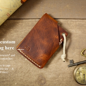 May include: A brown leather wallet with a white stitching detail and a white cord. The wallet has the initials "SB" embossed on the front. The text "Add free custom embossing here" is visible in the image. Choose max 5 characters and add in personalization box. *All letters are in caps. *Symbols available are . / & (one of each max).
