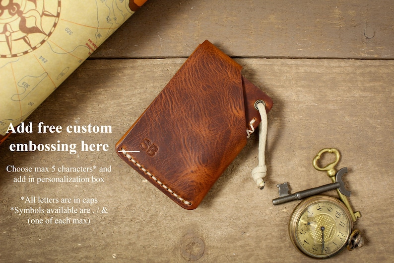 May include: A brown leather wallet with a white stitching detail and a white cord. The wallet has the initials "SB" embossed on the front. The text "Add free custom embossing here" is visible in the image. Choose max 5 characters and add in personalization box. *All letters are in caps. *Symbols available are . / & (one of each max).