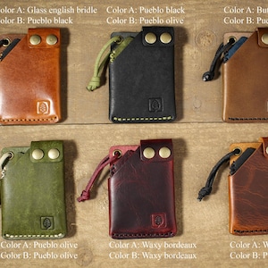 May include: Six leather card holders with different color combinations. Each holder has a small loop on the top and two brass rivets on the front. The holders are arranged in two rows of three.