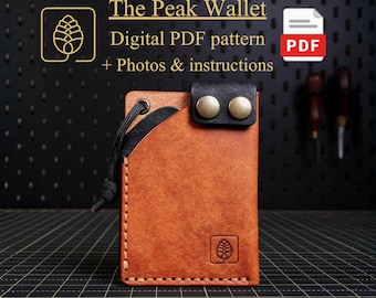 May include: A tan leather wallet featuring a black leather top flap with two brass-colored snap buttons, a black cord pull, and a pinecone logo embossed on the front. The text reads: The Peak Wallet Digital PDF pattern + Photos & instructions.