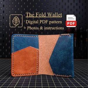 Può includere: Portafoglio in pelle aperto con pannelli blu e marroni, con il testo "The Fold Wallet" e "Digital PDF pattern + Photos & instructions". Il portafoglio è cucito con un filo a contrasto.