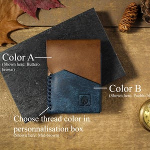 May include: A leather wallet with two different colored panels. The top panel is brown and the bottom panel is blue. The text "Color A - (Shown here: Buttero brown)" is above the top panel. The text "Color B - (Shown here: Pueblo blue)" is to the right of the bottom panel. The text "Choose thread color in personalisation box (Shown here: Mid-brown)" is below the wallet.